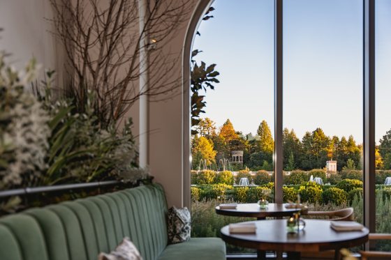 The interior of a restaurant featuring a sage green couch and tall arched ceilings. 